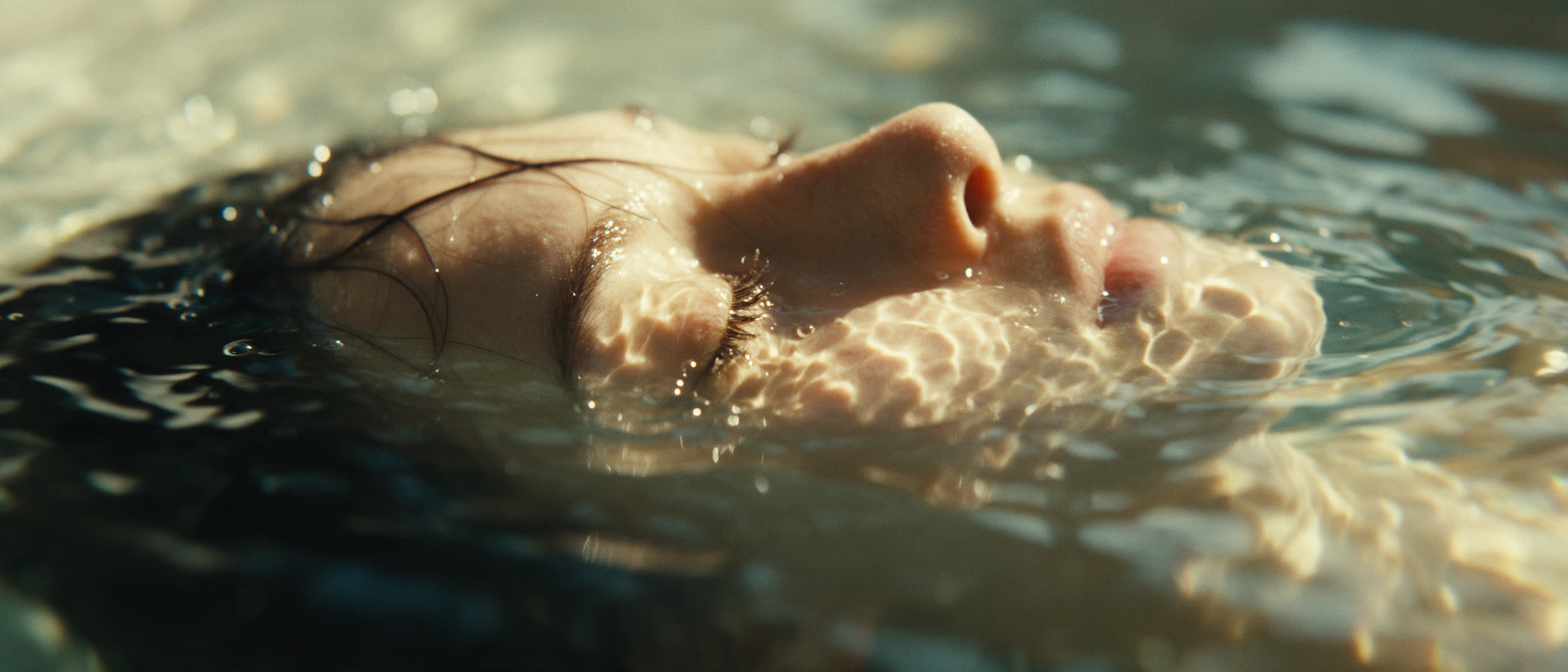 A face half-submerged in sunlit water, a frame from an aydya film